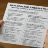 Person holding a printed infographic guide titled "New Zealand Embassy in UAE", detailing consular services, visa steps, contact info, and common mistakes